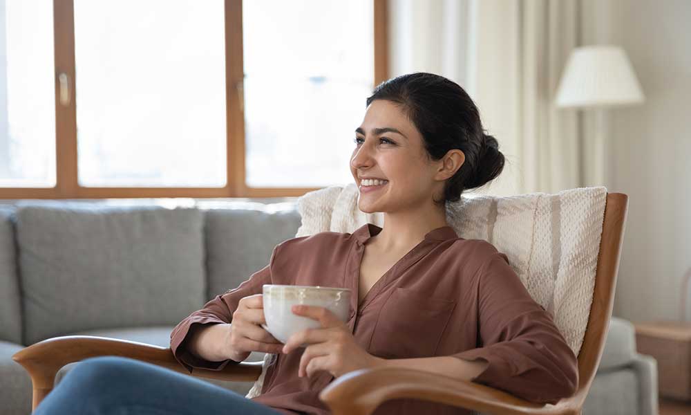A woman sat in a chair, holding a mug and smiling.