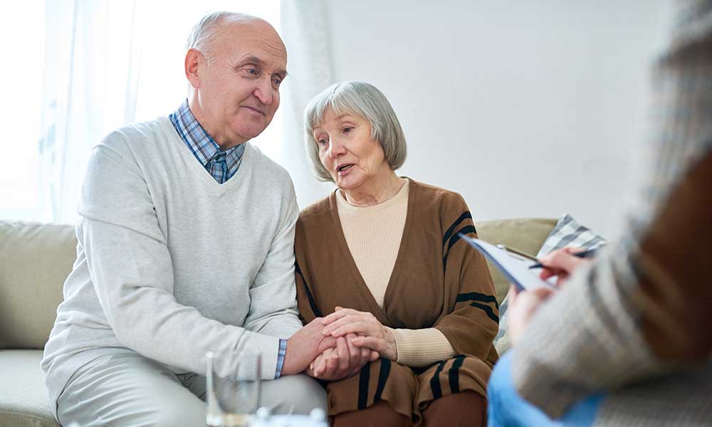 An older couple holding hands in a consultation room.