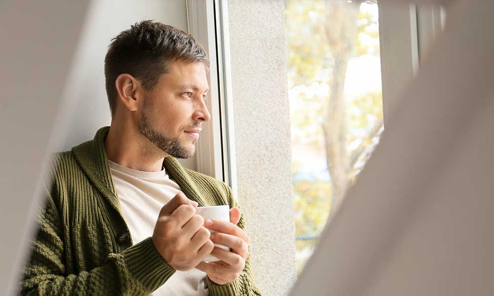 A man holding a mug whilst looking outside.