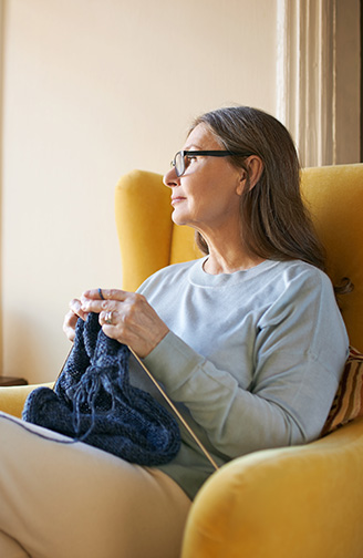 Portrait photo of a woman looking out the window whilst knitting.